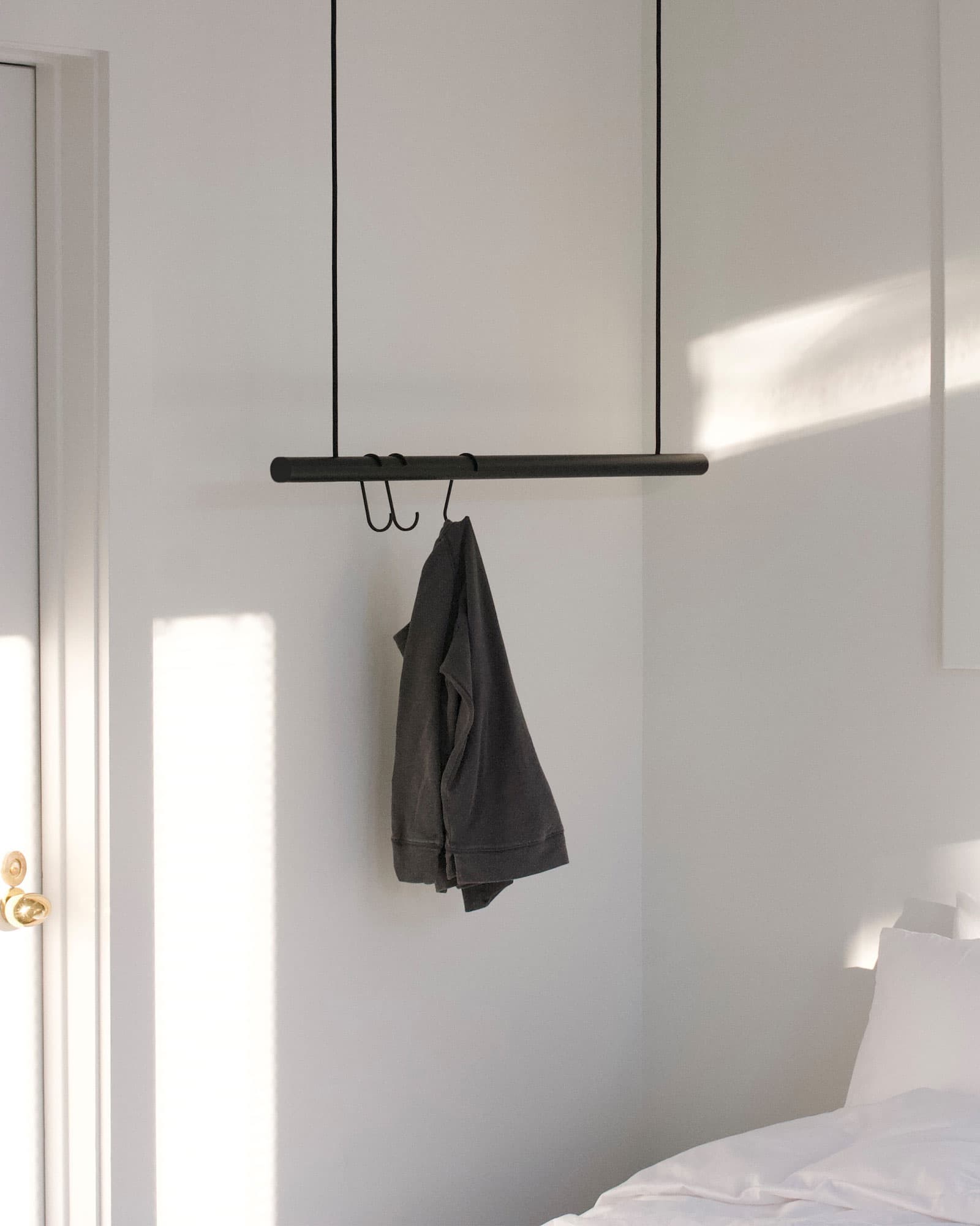 Hanging clothes rack with a gray garment against a white wall.