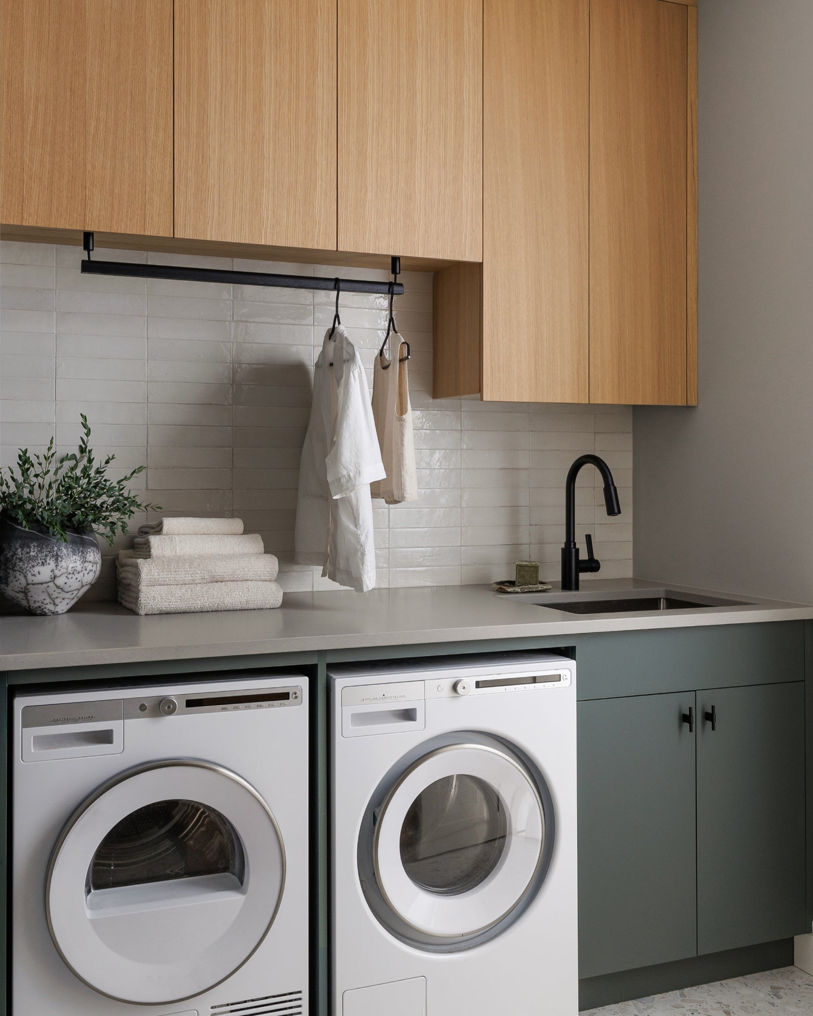 Modern laundry room with washing machine, dryer, and wooden cabinets.