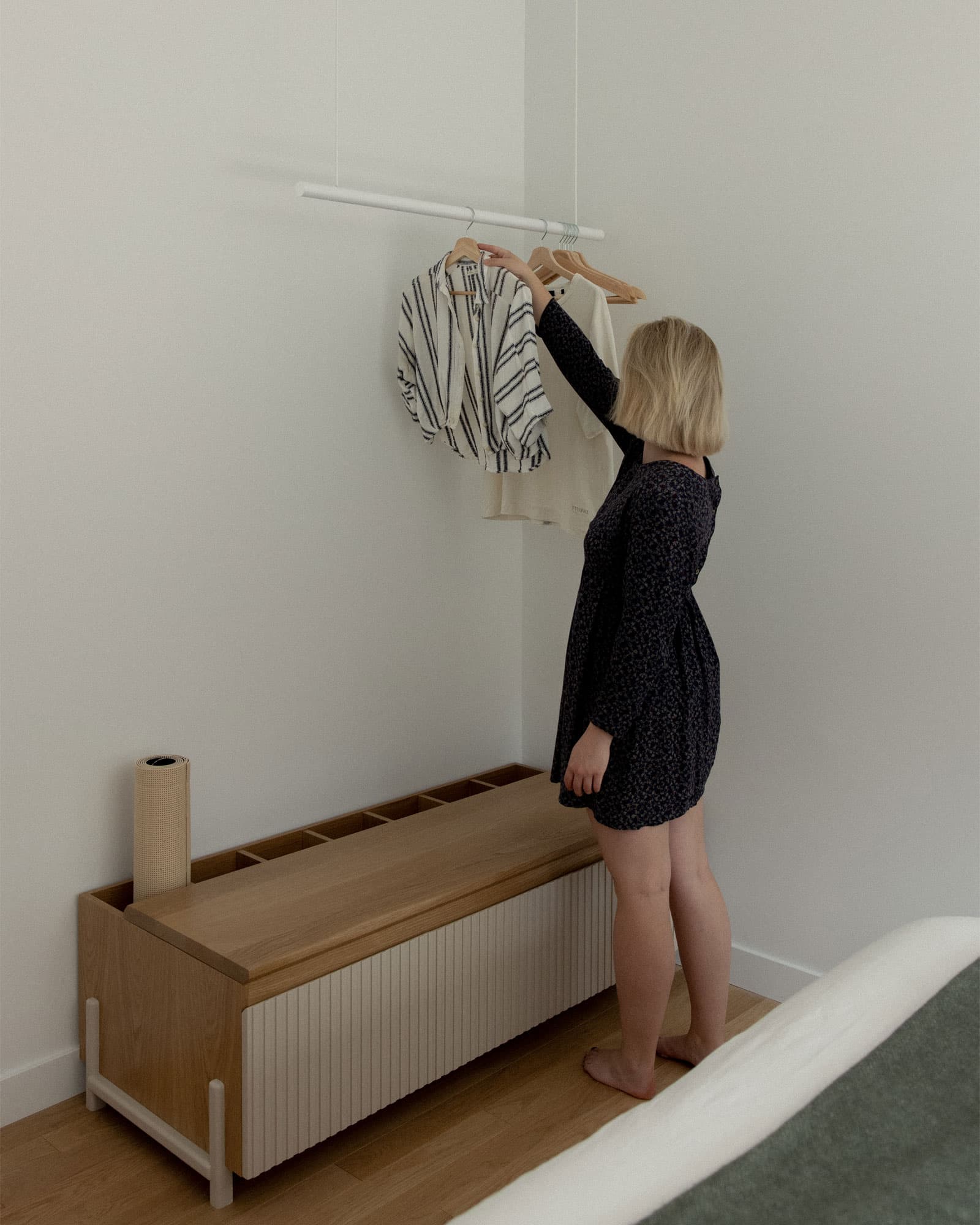 Person hanging clothes on a rack in a minimalistic room with wooden furniture.