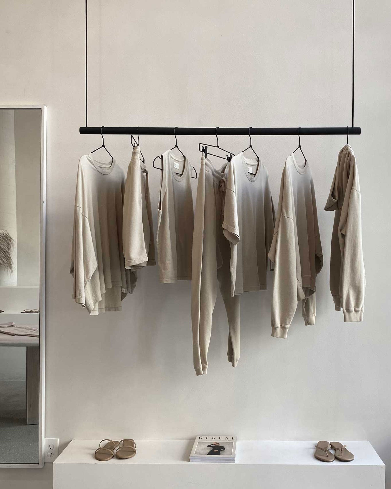 Beige shirts hanging on a rack against a plain wall with a small table and shoes in the foreground.
